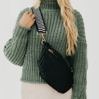 Woman wearing green knit sweater with black woven crossbody bag featuring striped strap