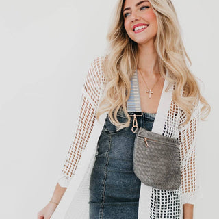 Woman wearing gray woven bum bag across chest with denim dress and white cardigan