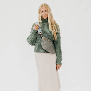 Woman wearing green turtleneck sweater and beige skirt with woven crossbody bum bag