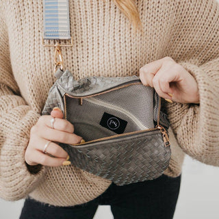 Person wearing beige sweater holding open woven crossbody bum bag with patterned interior lining