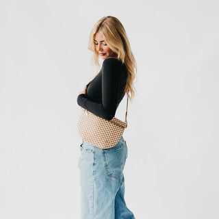 Woman wearing woven crossbody bum bag with black top and jeans against white background