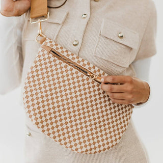 Person wearing cream outfit holding woven checkered bum bag with gold zipper and tan strap
