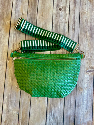 Green woven bum bag with striped adjustable strap and gold hardware on wooden background