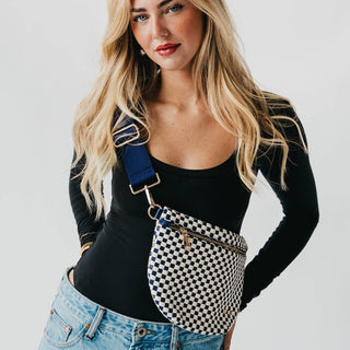 Woman wearing black and white checkered crossbody bum bag with blue strap over black top and jeans.