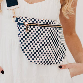 Woman wearing a checkered pattern woven bum bag with gold zipper across white dress