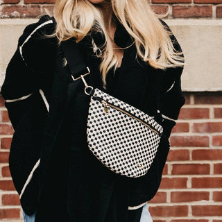 Person wearing black and white checkered woven bum bag across chest against brick wall background.