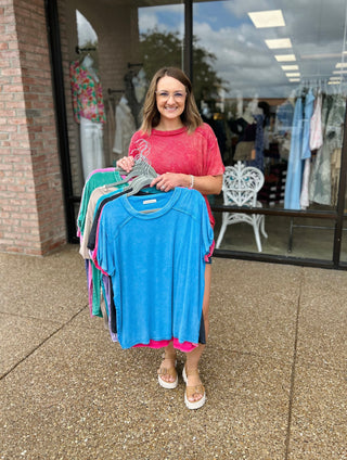 Woman holding colorful Zenana washed ribbed short sleeve tops on hangers outside clothing boutique storefront.