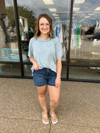 Woman wearing casual light blue ribbed short sleeve top with denim shorts outside retail store
