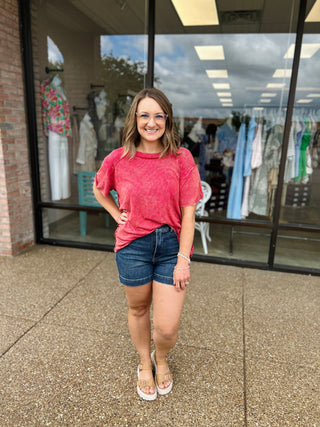 Woman wearing pink washed ribbed short sleeve top with denim shorts standing outside clothing store