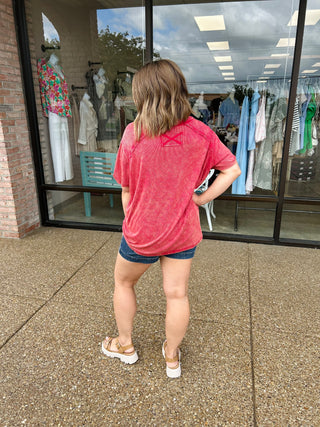 Woman wearing pink ribbed short sleeve top and denim shorts, standing outside clothing store window.