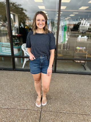 Woman wearing casual ribbed short sleeve top and denim shorts standing outside retail store