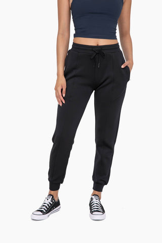 Woman wearing black cuffed joggers with drawstring waist and zipper pockets, paired with sneakers.