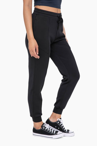 Woman wearing black joggers with zipper pockets and cuffed ankles, paired with black sneakers
