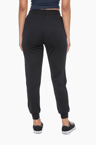 Woman wearing black cuffed joggers with zipper pockets and black sneakers, shown from behind.