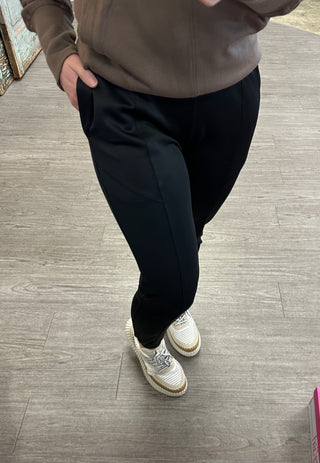 Person wearing black cuffed joggers with zipper pockets and sneakers on wooden floor